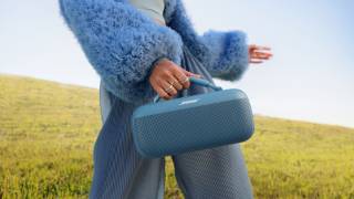 提着 Bose SoundLink Max 手提音箱穿过旷野的年轻女士