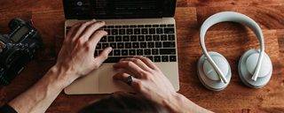 一位男士在办公桌前使用笔记本电脑工作时佩戴 Bose Noise Cancelling 700 无线消噪耳机