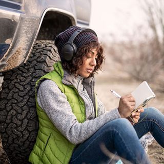 戴着 Bose QuietComfort 45 消噪耳机的女士靠在卡车上写日记