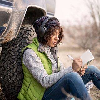 佩戴 Bose QuietComfort 45 消噪耳机的女士靠在卡车上写日记