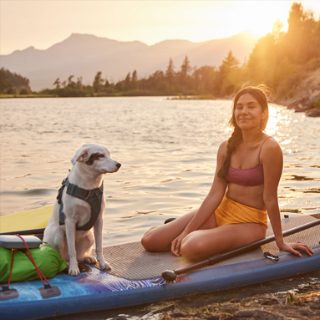 一位女士与她的狗坐在冲浪板上，一边听着 SoundLink Flex 蓝牙扬声器播放的音乐