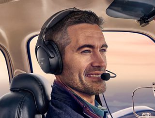 一位佩戴 Bose A30 航空耳机的飞行员坐在机舱中观看日出