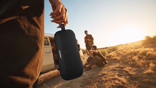 一位女士使用多用途绑带带着 Bose SoundLink Flex 便携式扬声器(第 2 代),坐在货车旁的一群朋友之中。