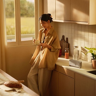 一位女士在厨房边喝咖啡，边欣赏从 Bose SoundLink Home 蓝牙扬声器流出的美妙音乐