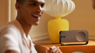 一位年轻男士正在聆听旁边桌子上的 Bose SoundLink Home 蓝牙扬声器播放的美妙音乐。