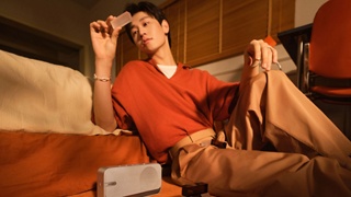 一位年轻男士坐在卧室地板上，靠着床边，聆听着 Bose SoundLink Home 蓝牙扬声器播放的美妙音乐。