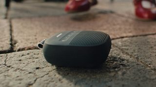 Bose SoundLink Micro 便携式扬声器 II 置于室外的地面上。
